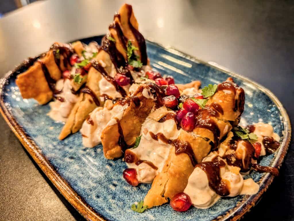 Samosa chaat on a blue platter drizzled with sauces and sprinkled with pomegranate